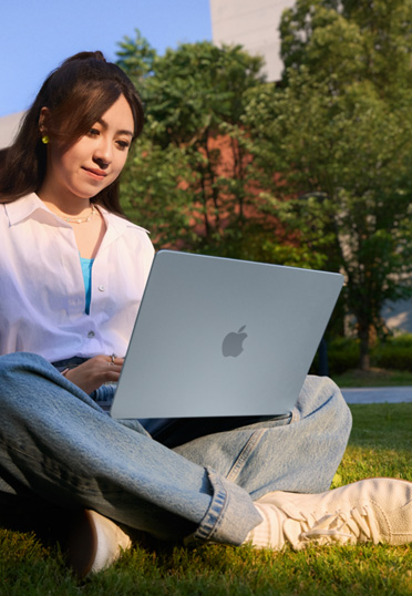 一名学生坐在户外。她腿上放着 MacBook。