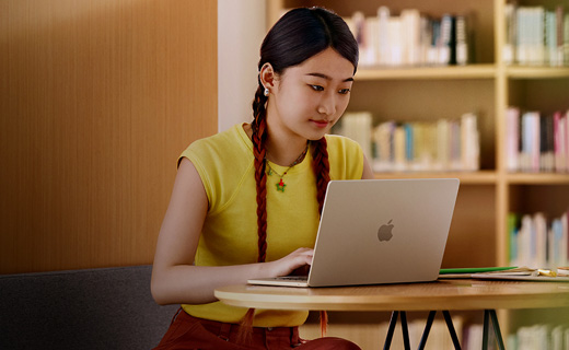 照片展示大学图书馆里，一位女生正坐在书桌前用着 MacBook Air。