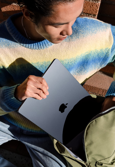 一名学生坐在外面。他从书包里拿出一台封闭的 MacBook。
